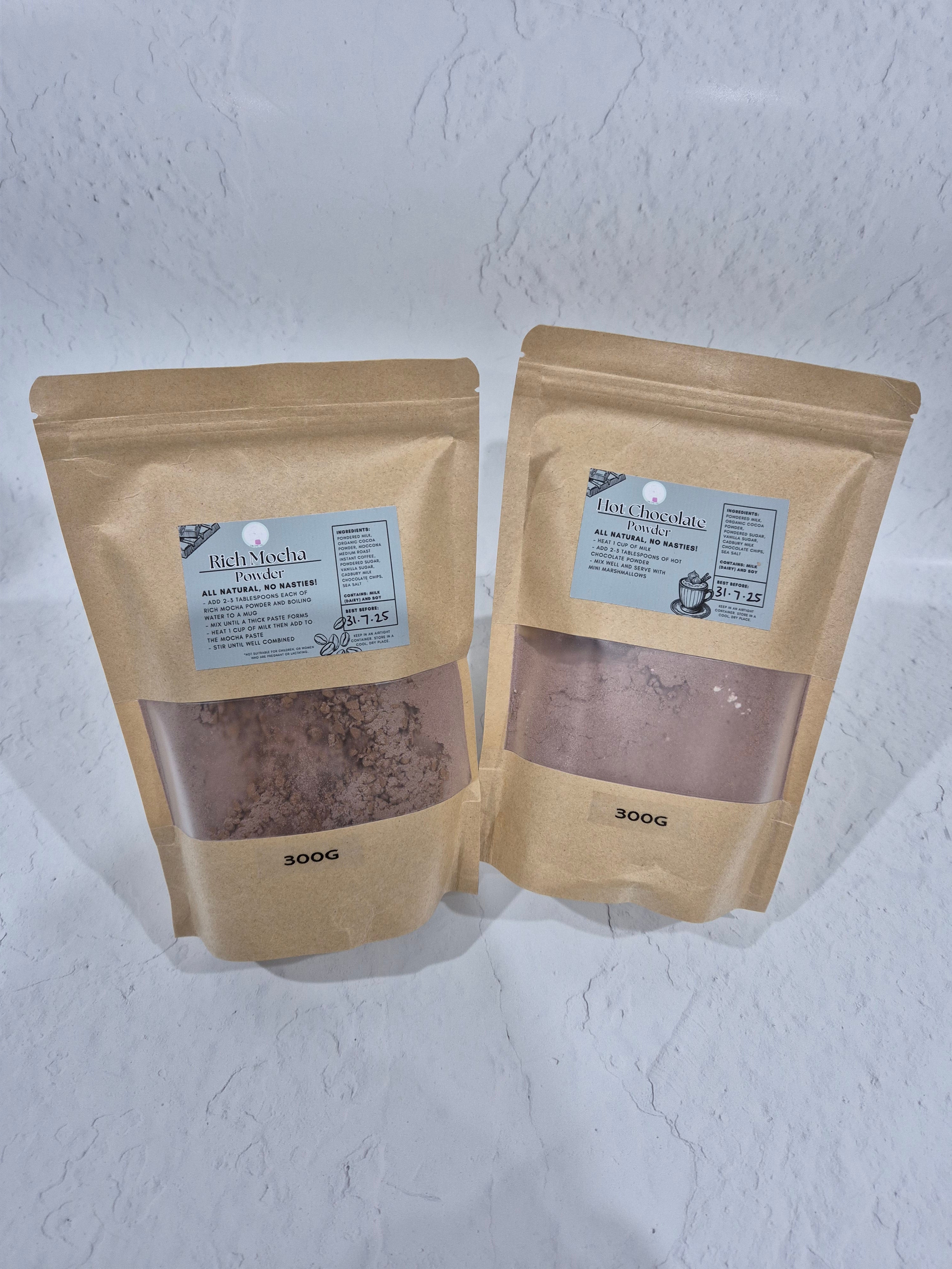 Pouches of Hot Chocolate and Rich Mocha powdered mixes in brown bags. Each displaying labels that identify the product by Baby Smash Cakes by Ange, the grams (300g) and the ingredient list for each.